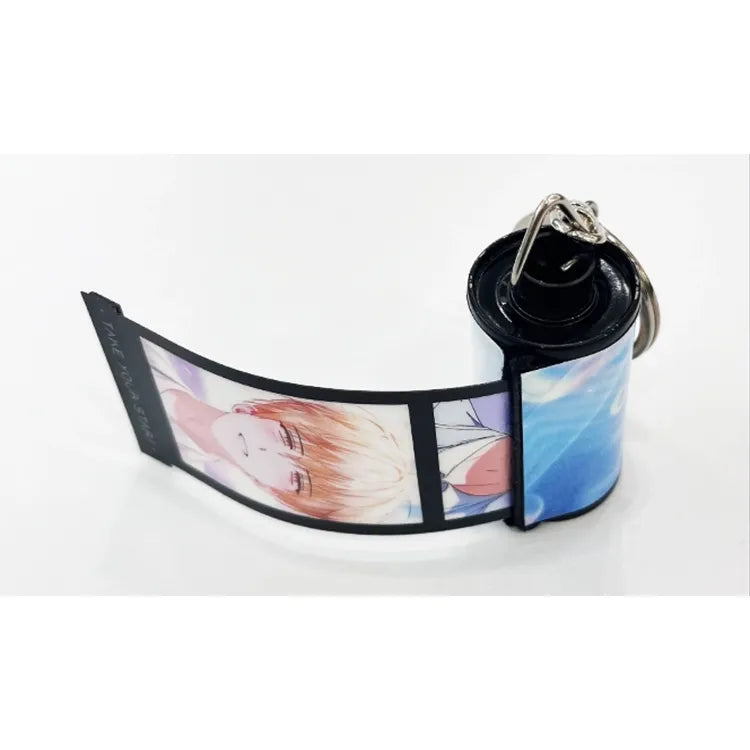 Debut or Die Film Roll Keychain featuring illustrated characters in intimate poses with light and dark backgrounds